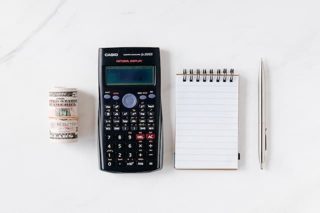a calculator, notepad, pen, and roll of money