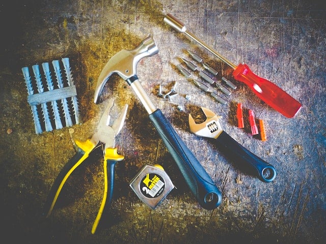 tools including a hammer, nails, pliers, and measuring tape laying on a surface