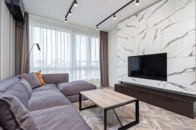 marble-walled living room with pruple-grey L-shaped couch and a tv