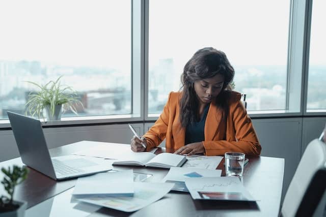 person in orange suit jacket working at their desk looking over documents