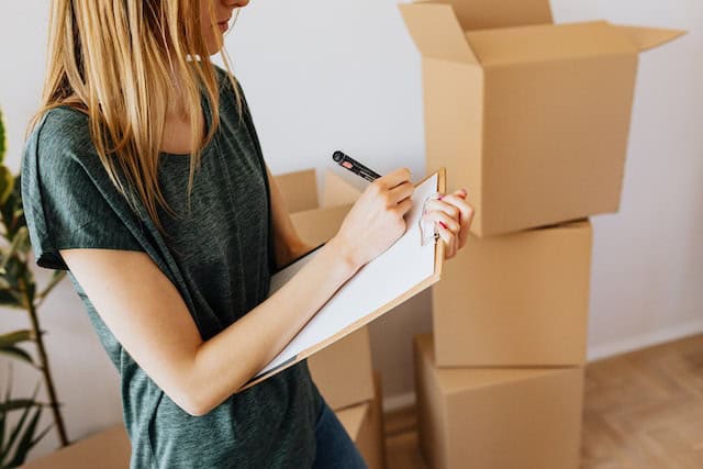 person-taking-notes-on-clipboard-with-cardboard-boxes-in-the-background