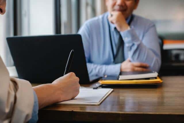 people-sitting-at-a-table-with-one-person-writing-something-on-a-piece-of-paper