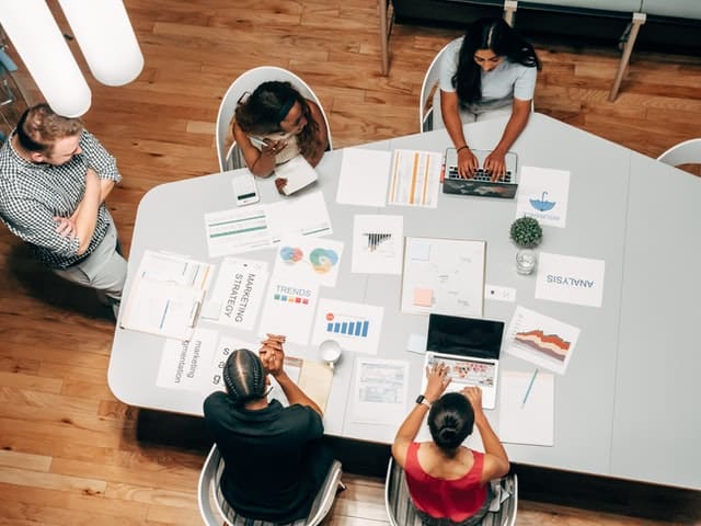 a-group-of-people-collaborating-at a-table-with-charts-laptops-and-documents-spread-out