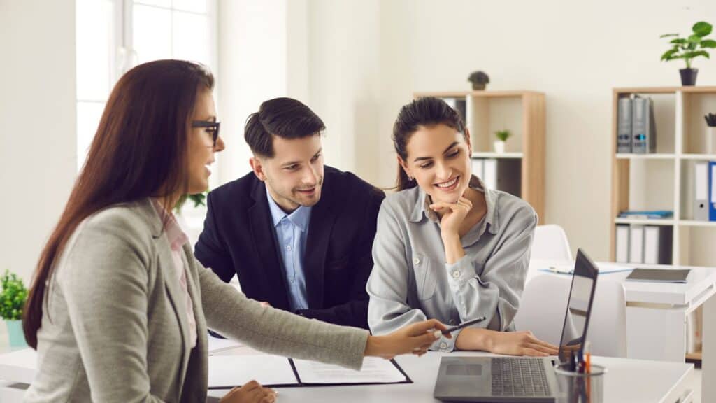 a-businesswoman-presenting-information-on-a-laptop-to-a-smiling-couple-in-an-office