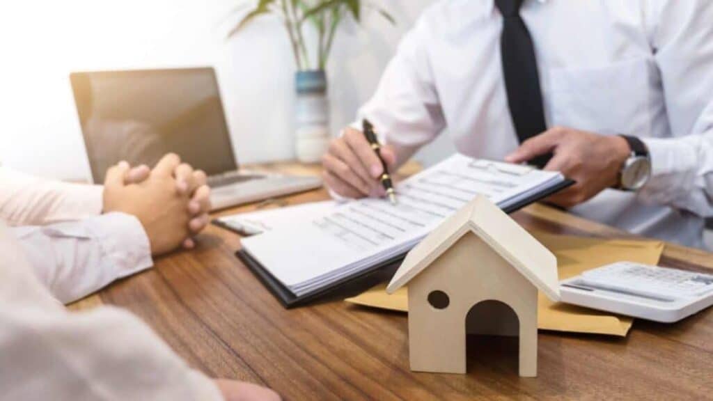 a-person-signing-a-real-estate-contract-with-a-small-wooden-house-model-on-the-table