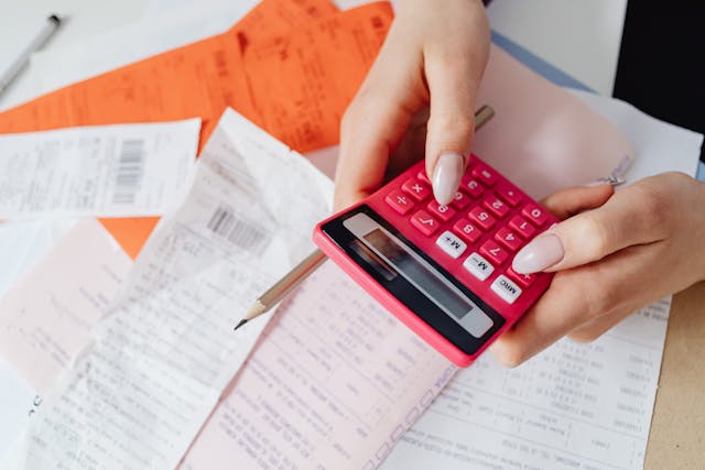 person-holding-a-red-calculator-and-pen-over-a-pile-of-receipts-and-financial-documents