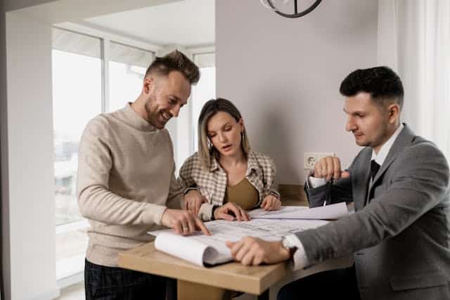 couple-sitting-at-table-looking-over-papers-with-landlord-in-a-suit